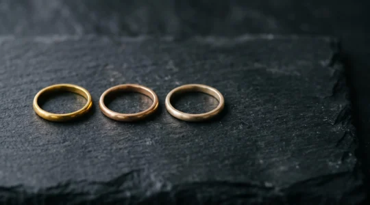 Tres anillos de oro con tonalidades doradas distintas representando los quilates 18k, 14k y 10k sobre una superficie oscura